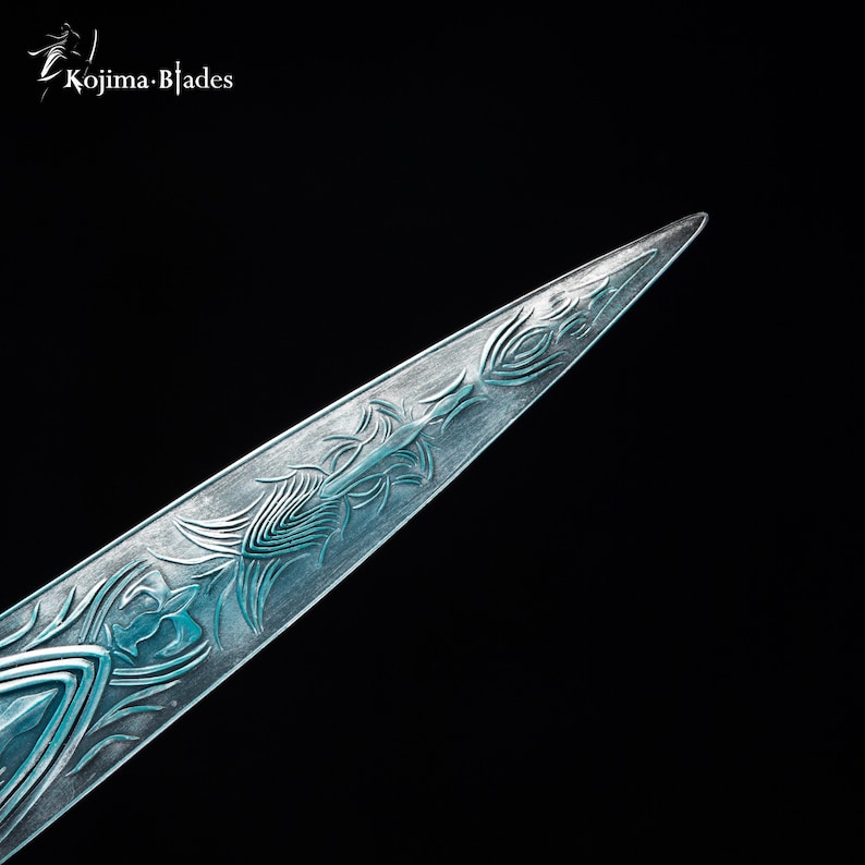 Puede incluir: Primer plano de la punta de una espada azul y plateada con intrincados dise&ntilde;os grabados en la hoja.