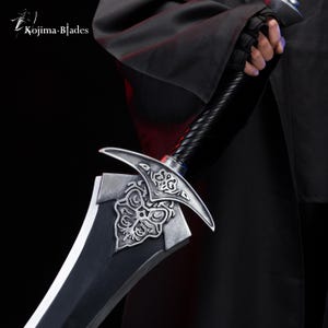 May include: A silver sword with a black handle and intricate floral designs on the blade. The sword is held by a gloved hand wearing a black cloak.