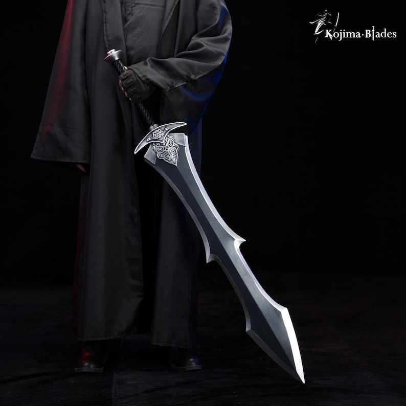 May include: A person in a black robe holds a large, silver sword with a detailed, ornate hilt. The sword has a black blade with a sharp point.