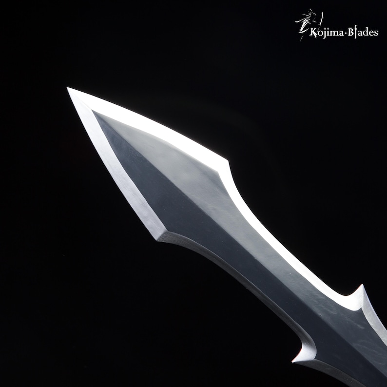 May include: Close-up of the sharp, pointed tip of a silver sword blade. The blade has a slightly curved, pointed tip and a straight edge.