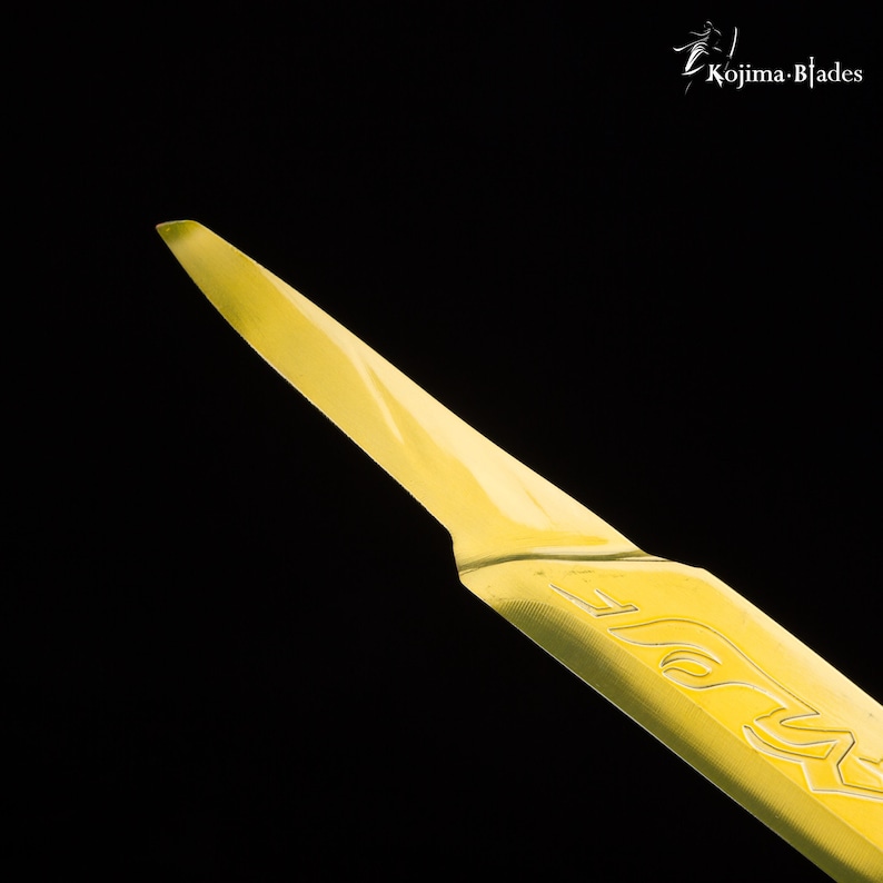May include: A close-up of a yellow, sharp, pointed blade with the word "KOJIMA" etched into the side.