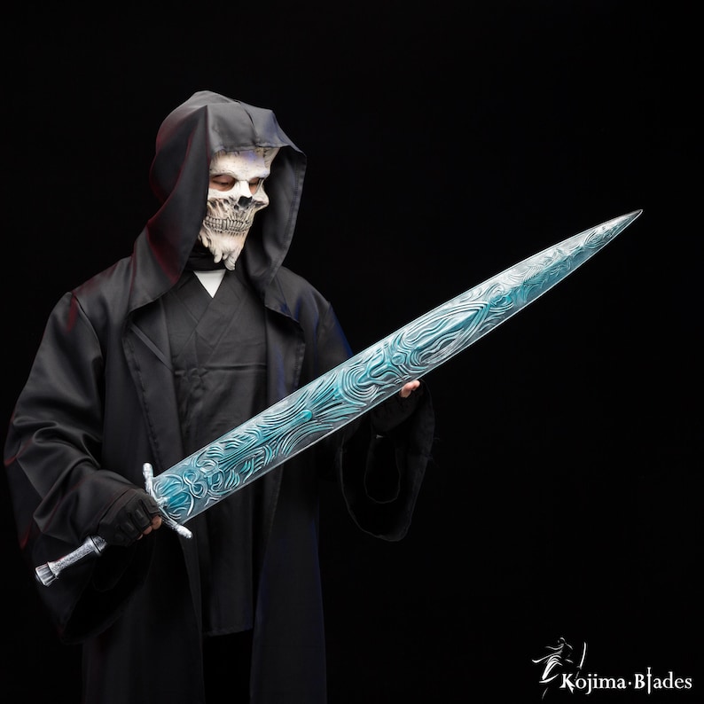 Puede incluir: Una persona con una t&uacute;nica negra con capucha y una m&aacute;scara de calavera blanca sostiene una espada larga, azul y plateada con dise&ntilde;os intrincados. La espada tiene una punta afilada y una empu&ntilde;adura plateada.