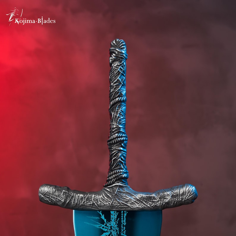 Op de afbeelding: Een close-up van het handvat van een zilveren zwaard met een blauw lemmet. Het handvat is gewikkeld in een getextureerd materiaal en heeft een donkergrijze afwerking.