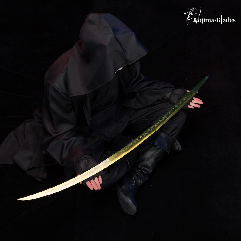 May include: A person wearing a black hooded robe holds a long, curved, gold-coloured sword with intricate green designs. The sword has a black handle and a sharp point. The background is black.