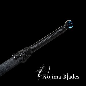 Może przedstawiać: Czarny miecz katana z głową smoka na rękojeści i niebieską szklaną kulą na końcu. Miecz jest ozdobiony skomplikowanymi wzorami.