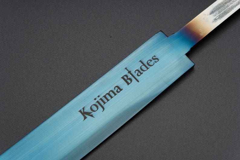 May include: A close-up of a blue steel blade with the text "Kojima Blades" etched into the surface.