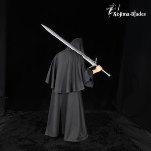 May include: A long, silver-colored metal sword with a detailed crossguard and pommel, held over the shoulder. The blade features etched markings near the hilt. The text Kojima Blades is visible in the upper right corner against a black background.