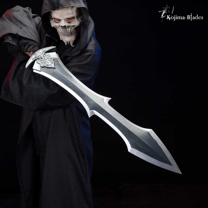 May include: A person wearing a black hooded robe and a skull mask holds a large, silver-colored sword with a decorative hilt. The sword has a sharp point and a double-edged blade.