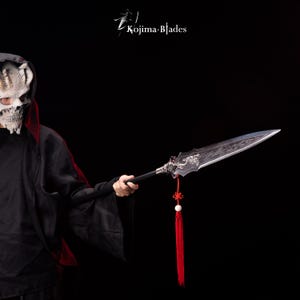 May include: A detailed spear with a silver blade and black handle. The blade features intricate carvings and a decorative dragon design. A red tassel hangs from the spear's handle. The text "Kojima Blades" is in the upper left corner.