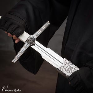 Könnte beinhalten: Ein silbernes Schwert mit einem verzierten Griff und einer doppelschneidigen Klinge. Das Schwert wird von einer behandschuhten Hand gehalten.