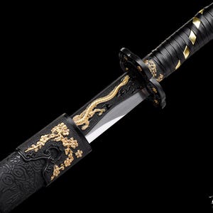 May include: Close-up of a Japanese katana. The black handle has a textured grip with gold details. The scabbard is black with gold floral patterns. The silver blade has a gold dragon design. The overall design is ornate.