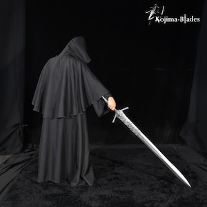 May include: A long, silver-colored metal sword with an intricate, textured hilt and crossguard, held by a figure wearing a black hooded cloak. The text Kojima Blades is visible in the upper right corner against a solid black background.