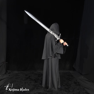 May include: A long, silver-colored metal sword with an ornate, detailed crossguard and hilt, held over the shoulder by a figure wearing a solid black hooded cloak. The blade is straight and pointed. The text Kojima Blades is visible.