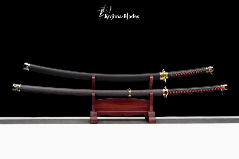 May include: Two black katana swords with red and black wrapped handles are displayed on a wooden stand. The swords are on a black background. The text "Kojima Blades" is visible in the top center of the image.