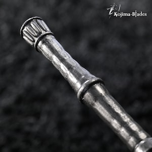 May include: A metallic silver-toned handle with a textured, bamboo-like appearance featuring segmented nodes and a fluted cap at the top end. The text Kojima Blades is visible in the upper right corner of the frame against a dark background.