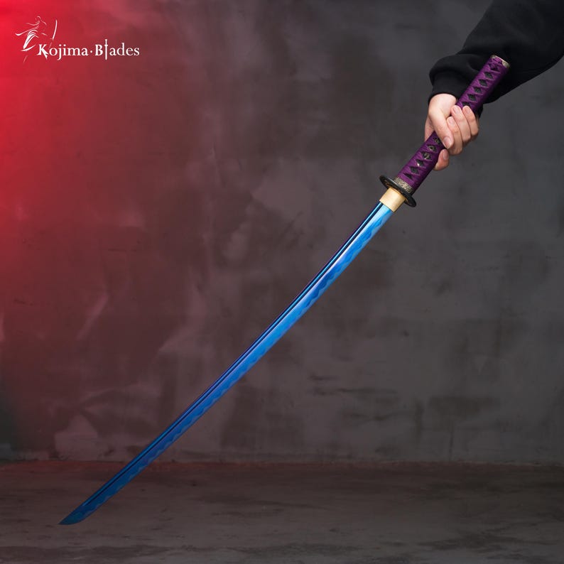 Pu&ograve; includere: Una katana blu con un'impugnatura viola e nera. La spada &egrave; tenuta da una mano su uno sfondo grigio.