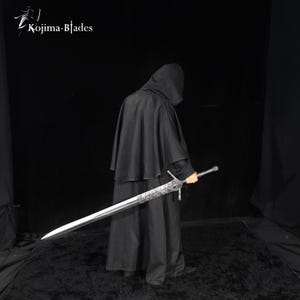May include: A long, double-edged steel sword with an intricate, etched pattern on the blade near the hilt. The sword features a straight crossguard and a textured grip. The Kojima Blades logo is visible in the upper left corner of the image.