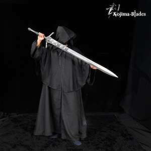 May include: A long, silver-colored metal sword with an ornate, textured crossguard and hilt, held horizontally. The sword features a pointed blade and intricate detailing on the guard. The Kojima Blades logo is visible in the top right corner.