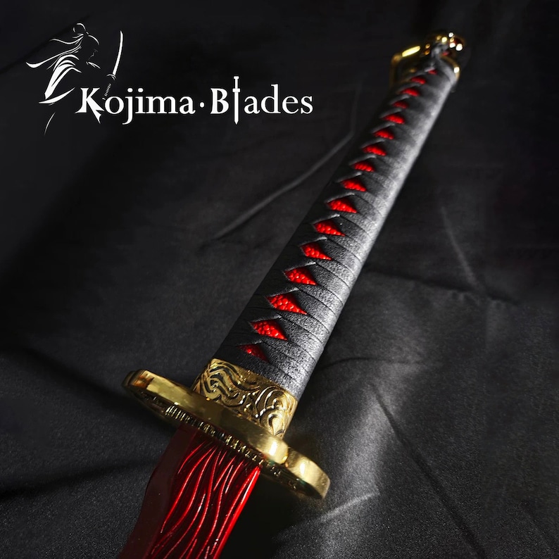 May include: A black and red katana sword with a gold-colored hilt and a red and black braided handle. The sword is on a black fabric background.