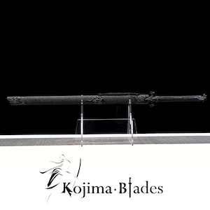 May include: A black katana sword with intricate dragon designs on the hilt and scabbard. The sword is displayed on a clear acrylic stand. The sword is labelled "Kojima Blades".
