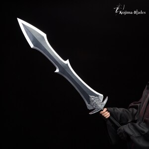 May include: A silver sword with a decorative handle and a sharp point. The sword is held by a person wearing a black robe.