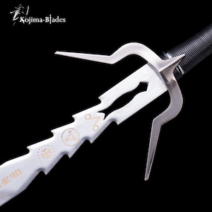 May include: A close-up of a silver sai, a traditional Japanese weapon. The sai features a pointed central prong and two curved side prongs. The blade has decorative cutouts and gold-colored symbols. The handle is black and textured.
