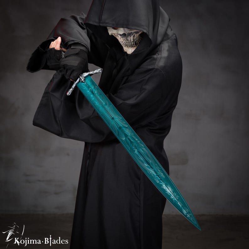 May include: A person wearing a black hooded robe holds a teal-colored sword with intricate designs. The sword has a silver hilt and a sharp point.