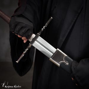 Könnte beinhalten: Ein silbernes Schwert mit einer schwarzen Lederscheide und einem gedrehten Metallkreuzschutz. Das Schwert wird von einer behandschuhten Hand gehalten.