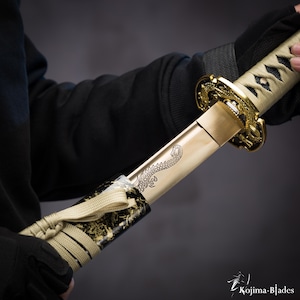 Puede incluir: Una katana de color dorado con una vaina negra y dorada. La espada tiene un diseño de dragón grabado en la hoja. La vaina está envuelta en un cordón beige.
