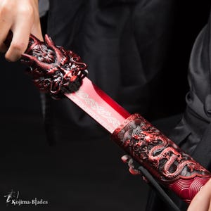 May include: A red sword with a dragon head handle and a dragon design on the scabbard. The sword is being held by a hand.