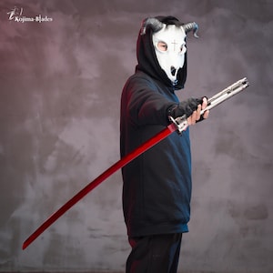 May include: A person wearing a black hoodie with a white skull mask with horns and a cross on the forehead, holding a red and silver katana sword.