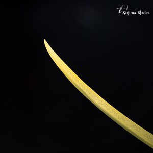 May include: A gold-coloured sword with intricate engravings on the blade. The sword is curved and has a sharp point.