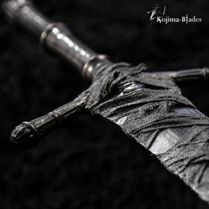 May include: A metallic sword with a dark, textured handle and a crossguard, featuring a blade partially wrapped in black fabric strips. The text Kojima Blades is visible in the upper right corner of the image, set against a dark background.