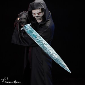 Puede incluir: Una persona con una t&uacute;nica negra con capucha y una m&aacute;scara de calavera blanca sostiene una espada larga, azul, con intrincados patrones. La espada se sostiene horizontalmente frente a la persona, con la punta apuntando hacia la derecha.