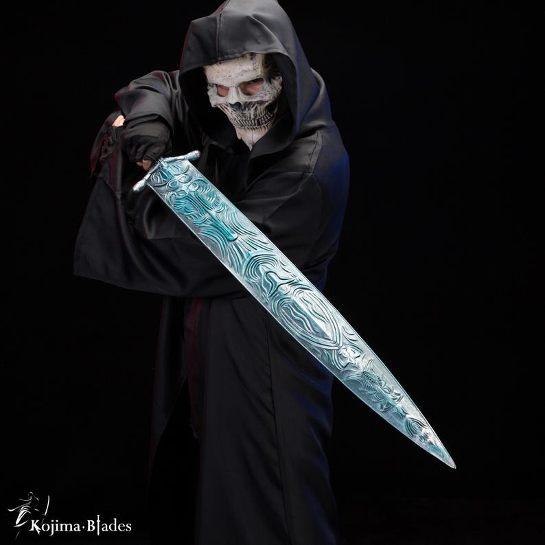 Puede incluir: Una persona con una t&uacute;nica negra con capucha y una m&aacute;scara de calavera blanca sostiene una espada larga, azul, con intrincados patrones. La espada se sostiene horizontalmente frente a la persona, con la punta apuntando hacia la derecha.
