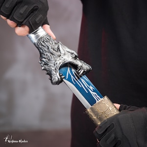 Op de afbeelding: Een zilveren zwaardknop met een wolfskop en een blauw en zilveren lemmet. Het zwaard wordt vastgehouden door een hand met een handschoen.