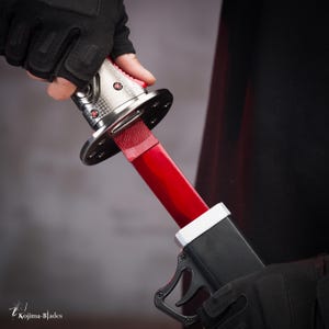 May include: A person is holding a red and silver katana sword with a black scabbard. The sword has a black handle and a red blade. The scabbard has a black handle and a silver metal ring.