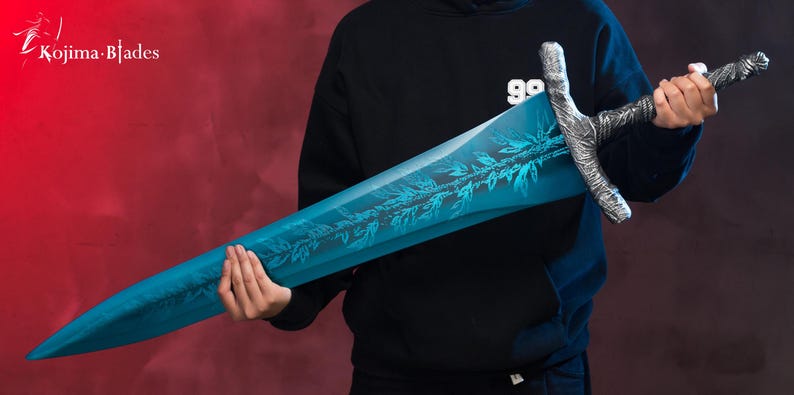 Op de afbeelding: Een blauw en zilveren zwaard met een gedetailleerd ontwerp op het lemmet. Het zwaard wordt vastgehouden door een persoon die een zwarte hoodie draagt.