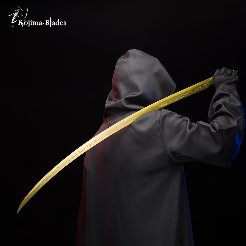 May include: A person wearing a black hooded robe holds a long, curved, gold-coloured sword with intricate engravings. The sword is held behind the person's back, with the tip pointing upwards.