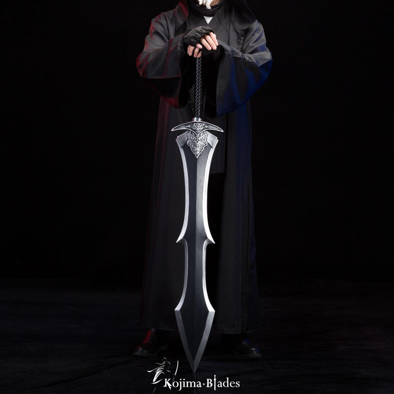 May include: A person in a black robe holds a long, silver sword with intricate details. The sword has a black handle and a pointed tip.