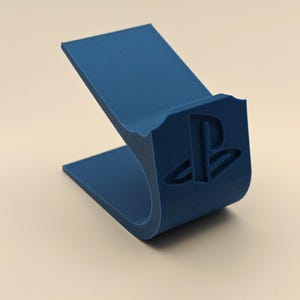 May include: A blue plastic stand for a PlayStation controller, featuring the PlayStation logo.