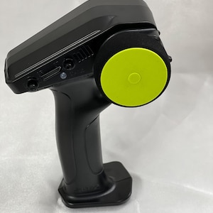 Può includere: Un telecomando nero con un pulsante giallo sulla parte superiore. Il telecomando ha un'impugnatura testurizzata e una base nera con la parola "Blitz" stampata su di essa.