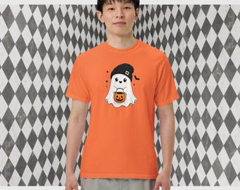 May include: An orange short-sleeved t-shirt featuring a graphic of a white ghost wearing a black beanie and holding a small orange jack-o'-lantern bucket. The ghost design includes small black hearts, stars, and a bat silhouette on the side.