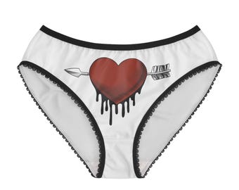 May include: White underwear featuring a black trim and a central graphic of a red heart pierced by an arrow with black liquid dripping from the bottom of the heart. The design has a cross-hatched texture and a bold, dark aesthetic throughout.