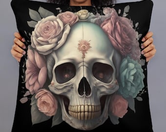 May include: Black square pillow featuring a skull design adorned with a floral crown of pink, peach, and teal flowers. The skull has a light blue-green hue and a small floral design on the forehead. The pillow is held by a person.