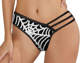 May include: Black and white underwear featuring a spider web pattern across the front panel. The garment includes a scalloped trim along the top edge and three thin black elastic straps extending from the side to the back of the waistband.