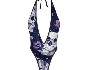 May include: A deep-cut halter bodysuit featuring a dark navy blue background with a swirling pattern. The garment is decorated with a repeating print of white human skulls and light purple flowers, finished with black trim along the edges.