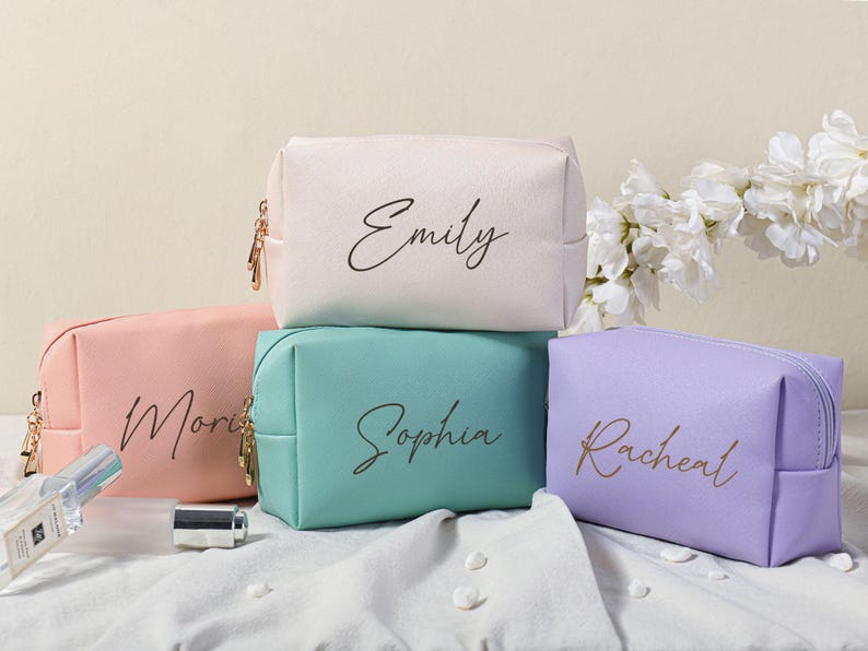 Puede incluir: Cuatro bolsas de cosm&eacute;ticos personalizadas en diferentes colores. Las bolsas est&aacute;n hechas de un material suave y texturizado y tienen un cierre de cremallera. Las bolsas est&aacute;n etiquetadas con los nombres "Emily", "Sophia", "Rachel" y "Morgan".
