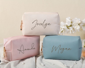 Peut inclure: Trois trousses de toilette personnalisées avec des fermetures à glissière. Les trousses sont en rose, blanc et bleu avec les noms Amanda, Jocelyn et Megan écrits en cursive noire.