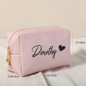 Puede incluir: Una bolsa de cosm&eacute;ticos rosa con una cremallera dorada y el nombre "Dorothy" impreso en negro con un peque&ntilde;o coraz&oacute;n negro. La bolsa mide 16 cm por 9 cm.